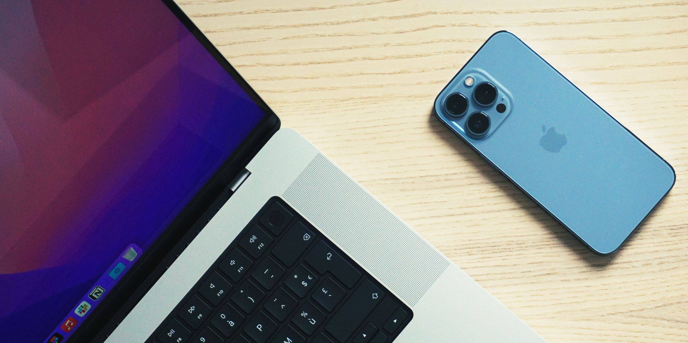 A top down view of a MacBook Pro and in iPhone on a desk.