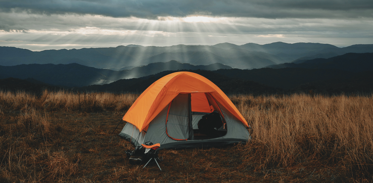 A small tent in the middle of mountains with a small matching stool set outside.
